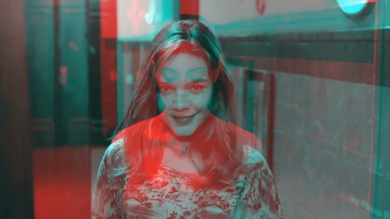 A young woman with long hair and a floral dress walks towards the camera, then transforms into an older woman holding a plate of brownies, in a hallway with red and blue lighting.