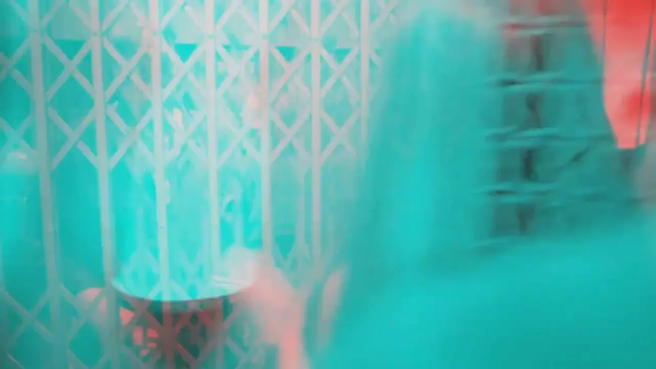 A young man and woman are seen in a blurry, color-separated shot, embracing and kissing passionately in an interior setting.