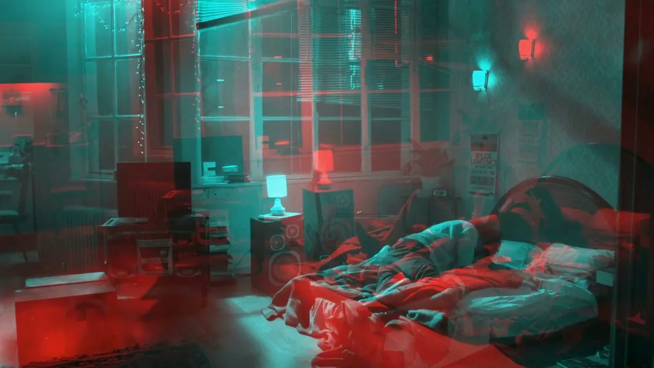 A young man in his 20s is sleeping in a messy bedroom with red and blue lighting, as the camera slowly pushes in.