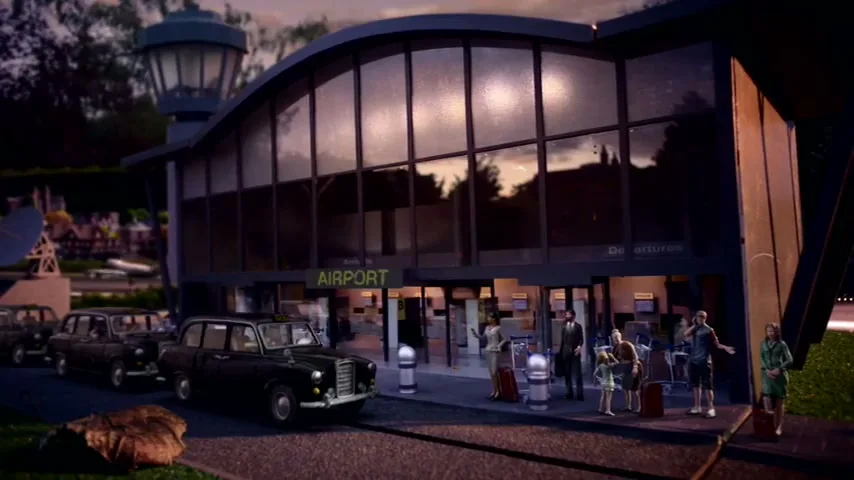 A miniature airport terminal with several miniature people and black taxi cabs outside, under a twilight sky.