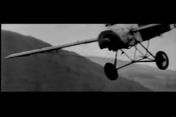 A black and white shot shows a small, vintage airplane flying through the sky, with a pilot visible in the cockpit.