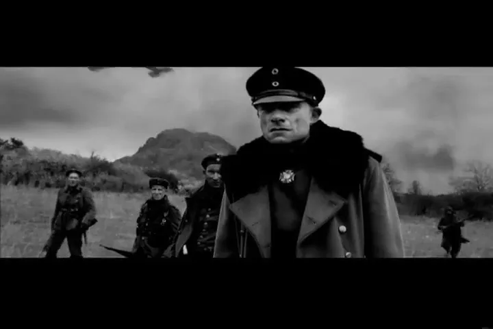 A group of soldiers in military uniforms walk across a field towards the camera, with a crashed plane in the background.