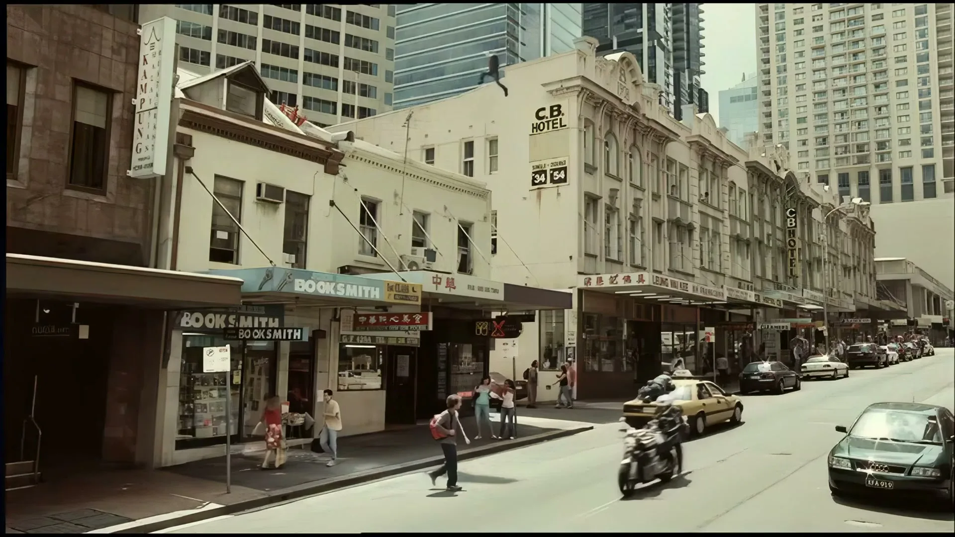 A wide shot of a bustling city street with pedestrians, cars, and a motorcycle, featuring old buildings and modern skyscrapers in the background.