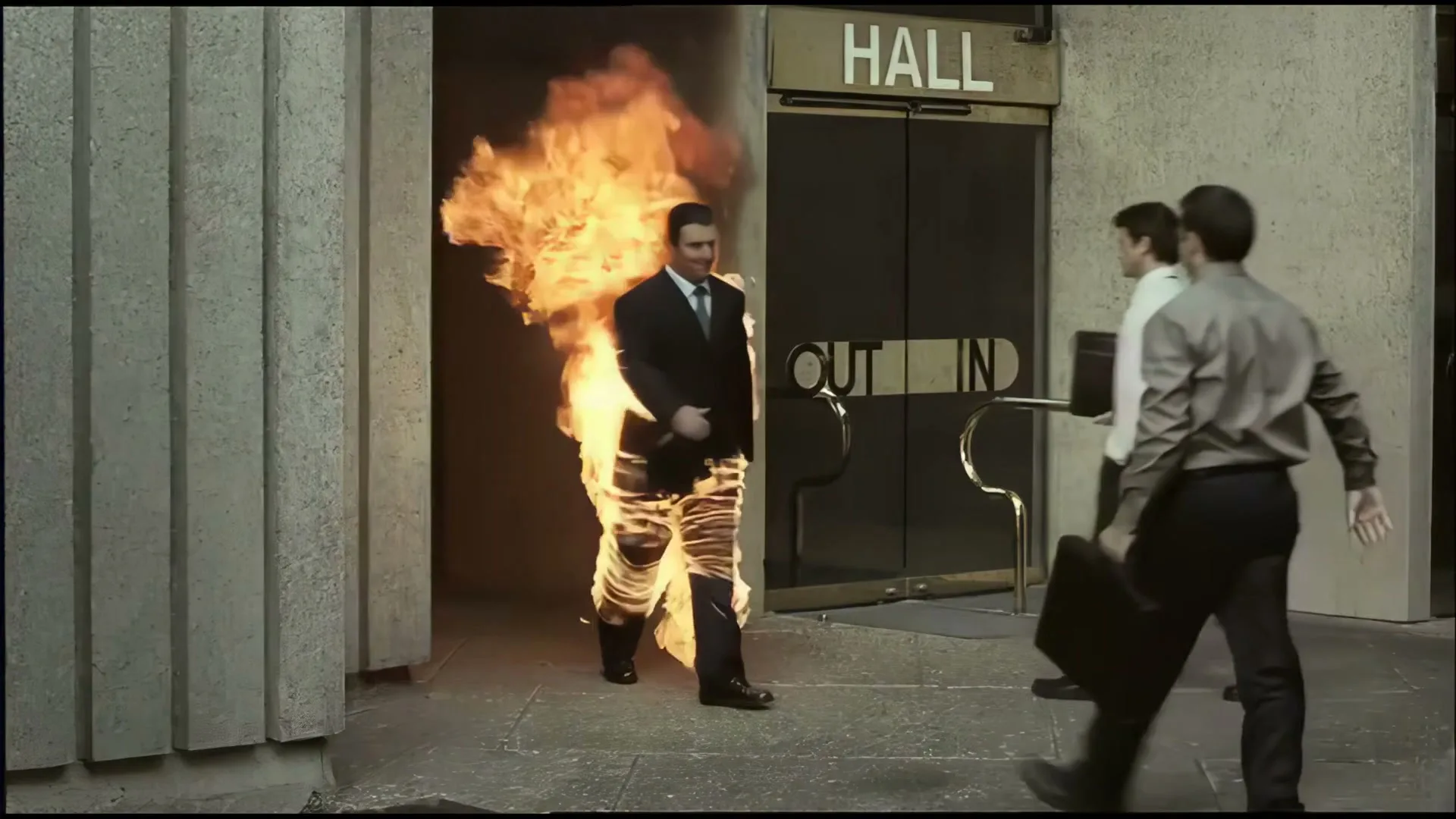 A man in a suit, engulfed in flames, walks out of a building labeled "HALL" as two other men walk past him, seemingly unfazed.