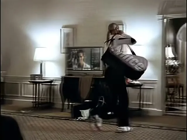 Maria Sharapova, a young female tennis player, walks through a hotel room with a tennis bag over her shoulder, preparing to leave.