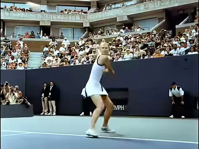 Maria Sharapova, a blonde female tennis player in a white dress, hits a forehand on a tennis court during a match in a stadium.