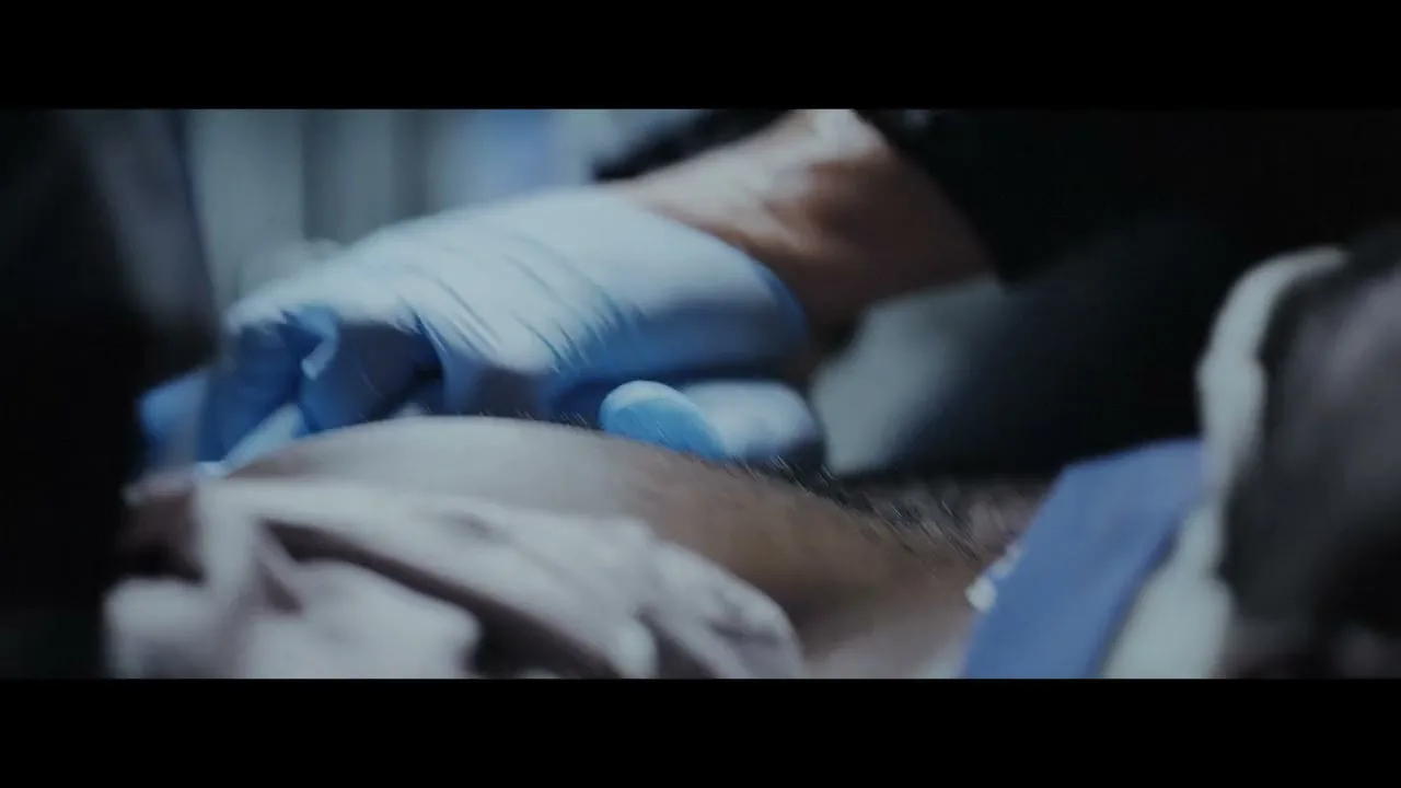 A person in blue gloves performs CPR on another person's chest in a dimly lit, intense interior setting.