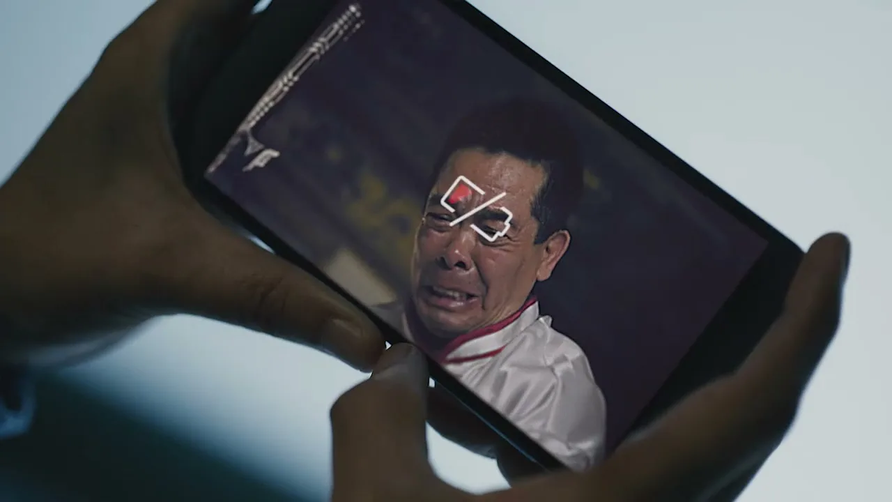 A person holds a smartphone displaying a crying man with a low battery icon over his eyes, in an interior setting.