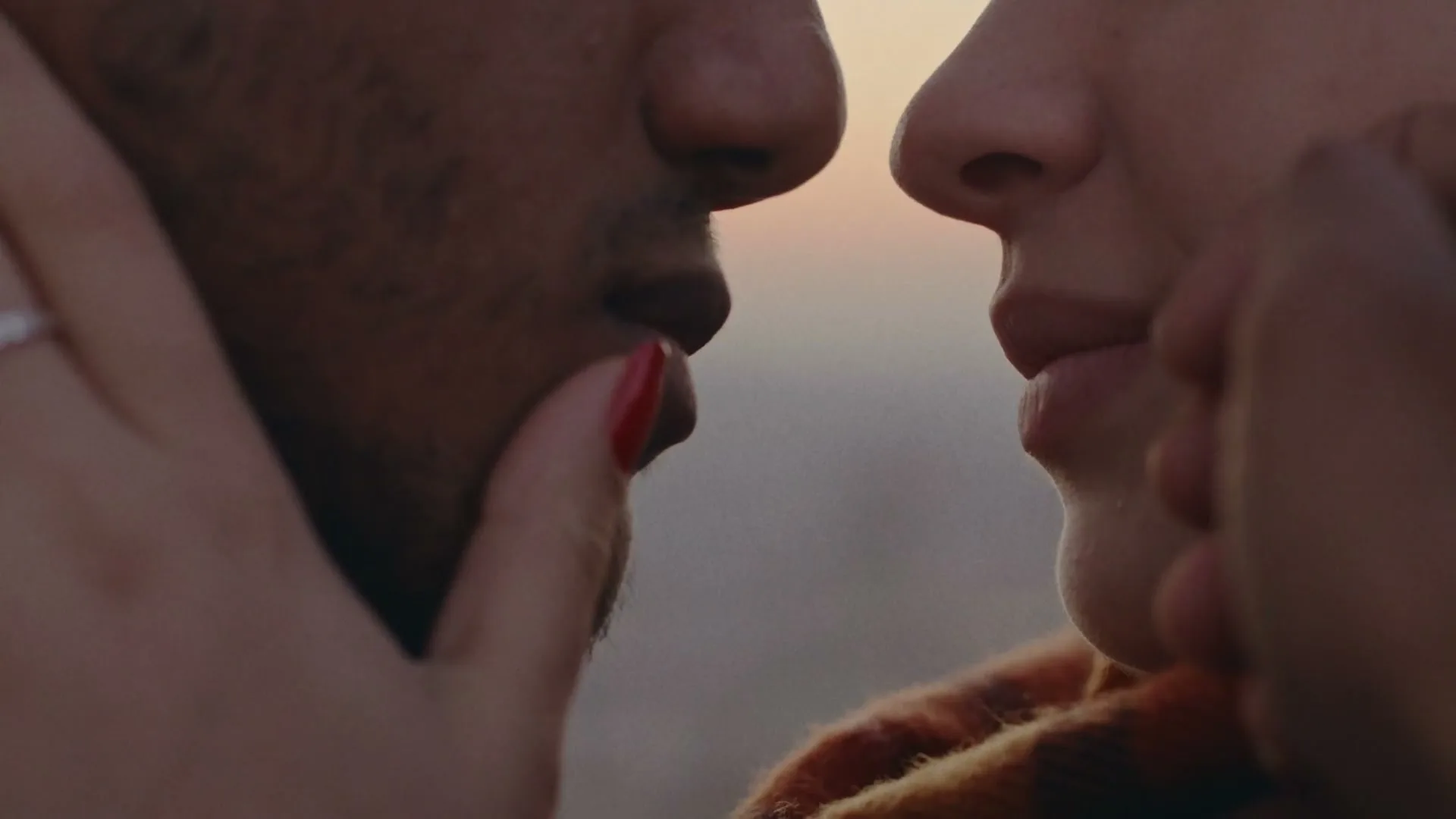 A man and woman are seen in a close-up, almost touching noses, with the woman's hand gently caressing the man's face during golden hour.