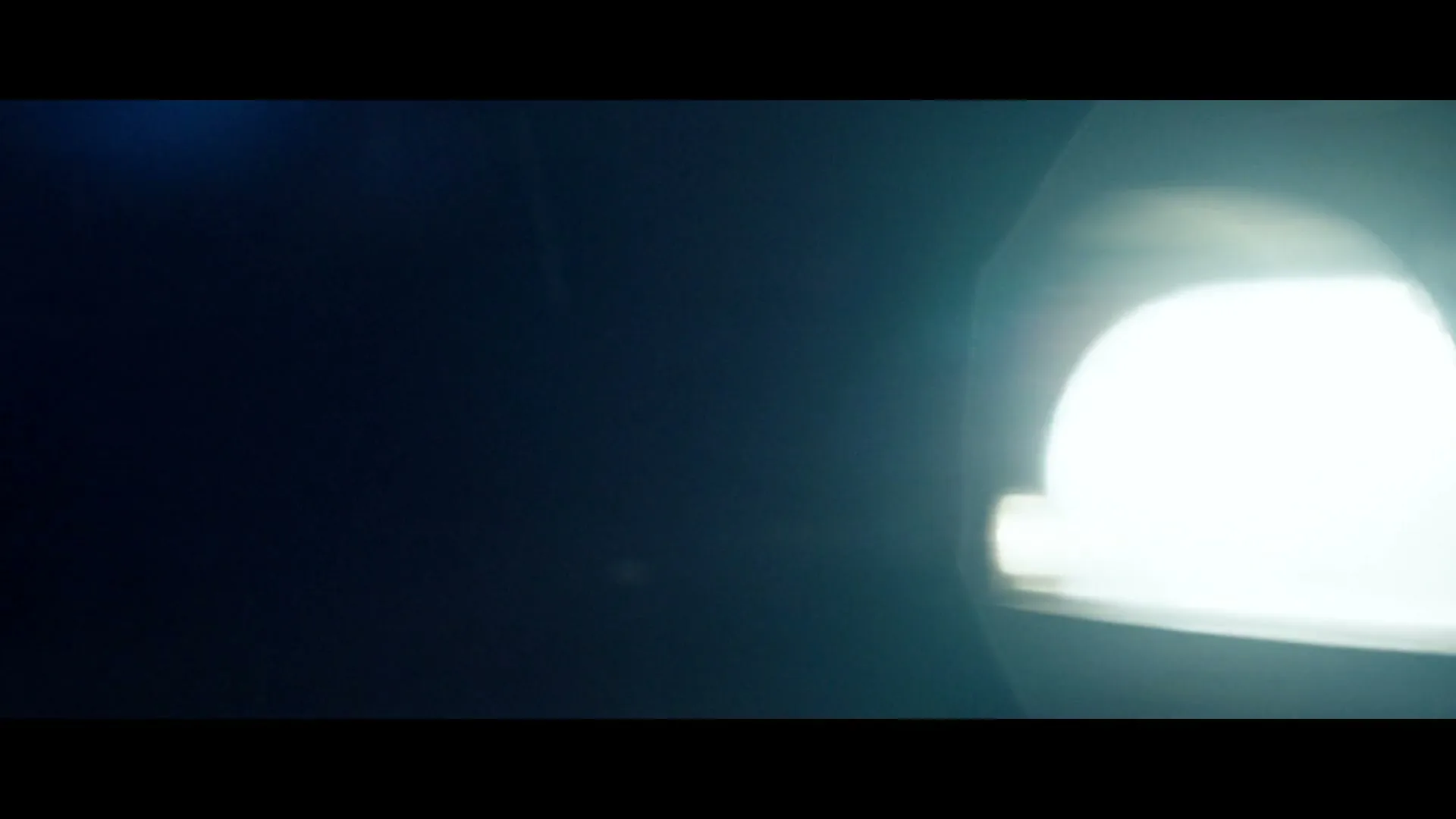 A bright car headlight and part of a dark car grille are visible as the camera quickly moves past, creating a blur.