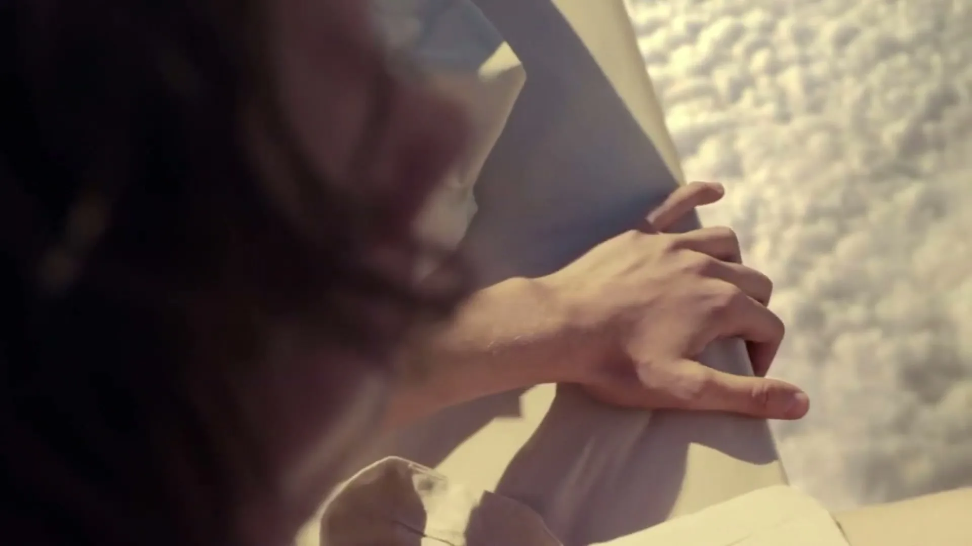A person's hand gently touches a bedsheet, with soft light illuminating the scene, suggesting comfort and tranquility.