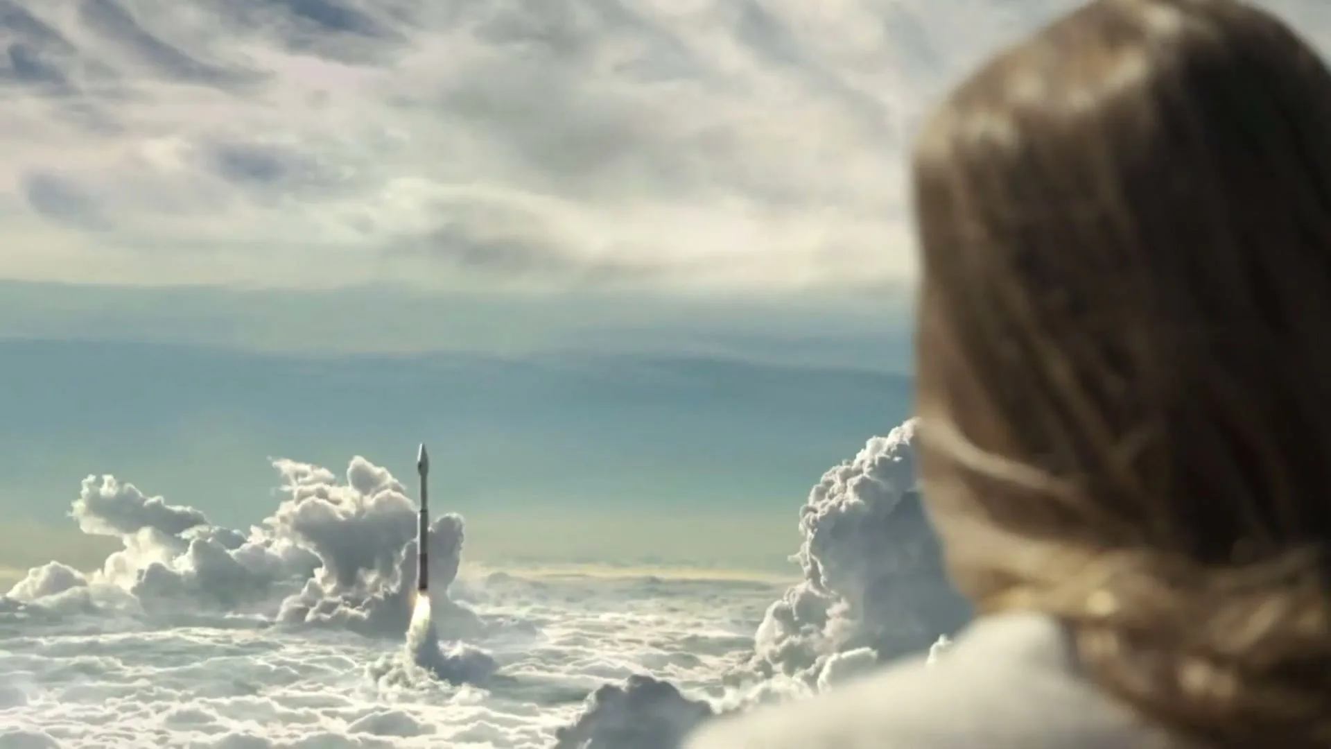 A young woman with long brown hair watches a rocket launch into the sky from above the clouds.