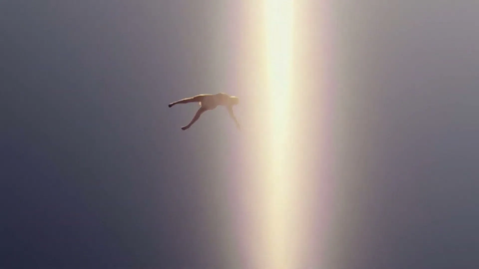 A person is seen from above, floating in a dark void with a bright vertical beam of light shining down on them.