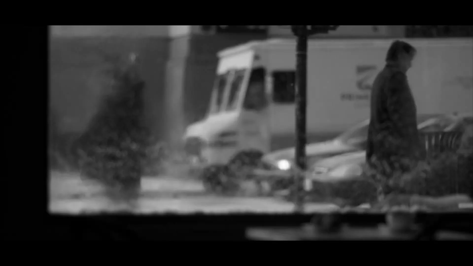 A man walks past a window, then the camera pans down to a street grate with steam rising from it, in a black and white urban setting.