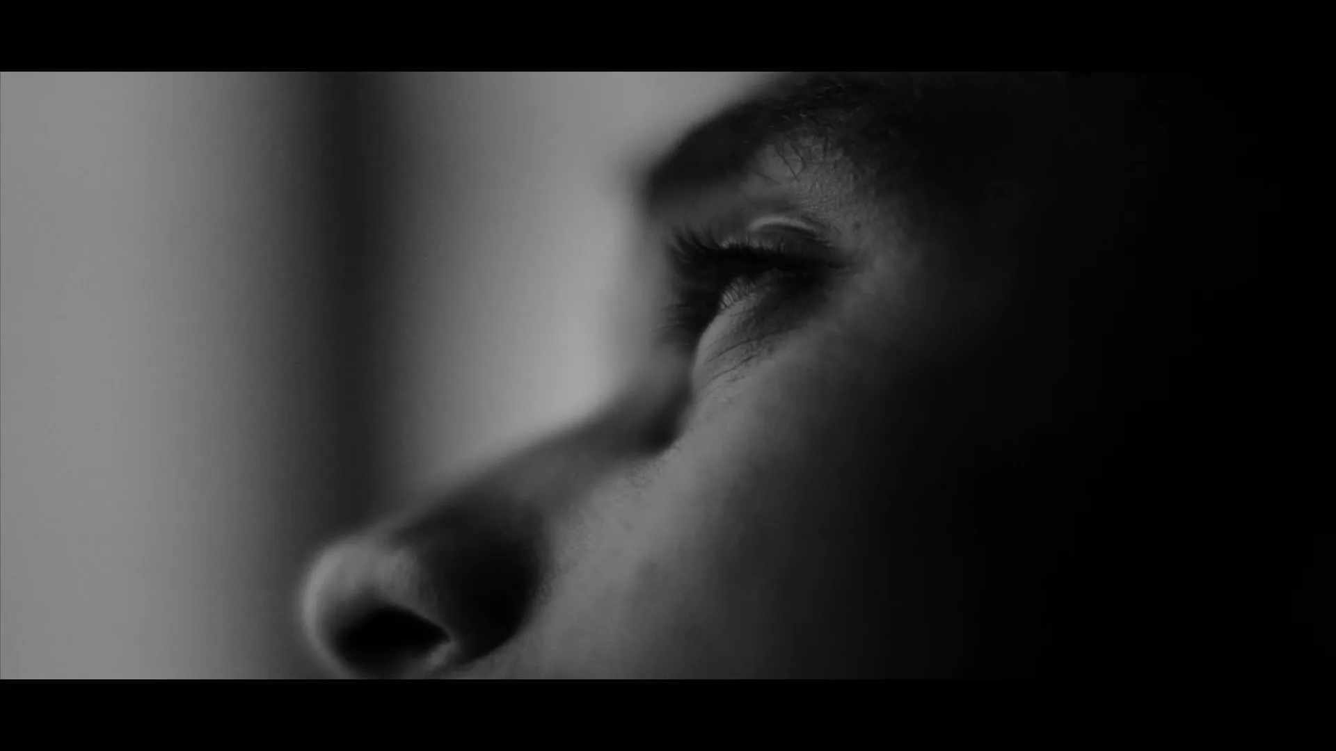 A black and white extreme closeup of a person's eye and nose, looking up and to the right, with soft light on their face.