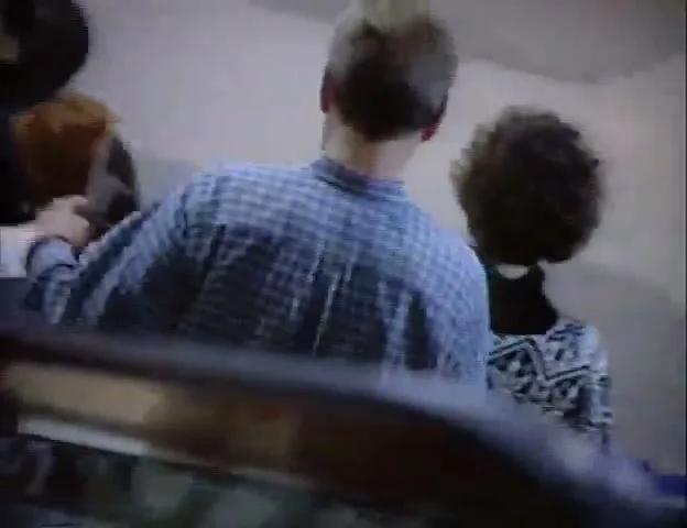 A bald man in a suit and tie looks around while riding an escalator with other people in an airport terminal.