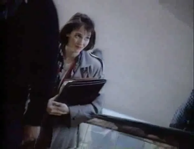 A woman in a trench coat holds a folder and smiles while riding an escalator in an airport.