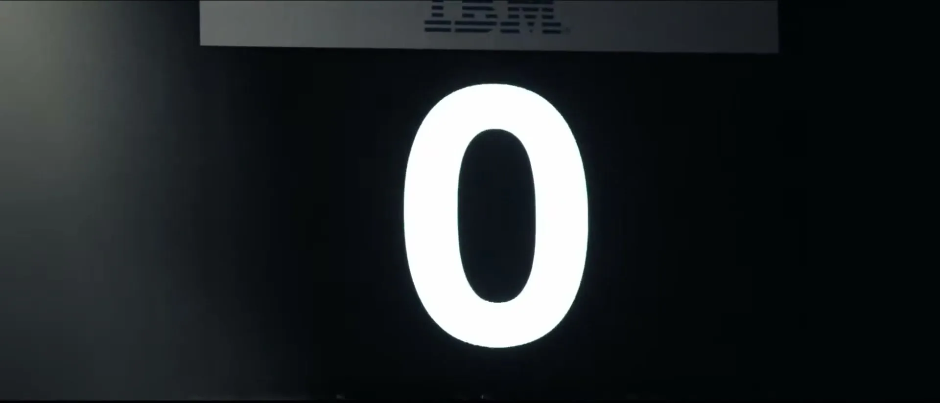 A white number zero transforms into a geometric pattern on a dark screen, with an IBM logo visible at the top.