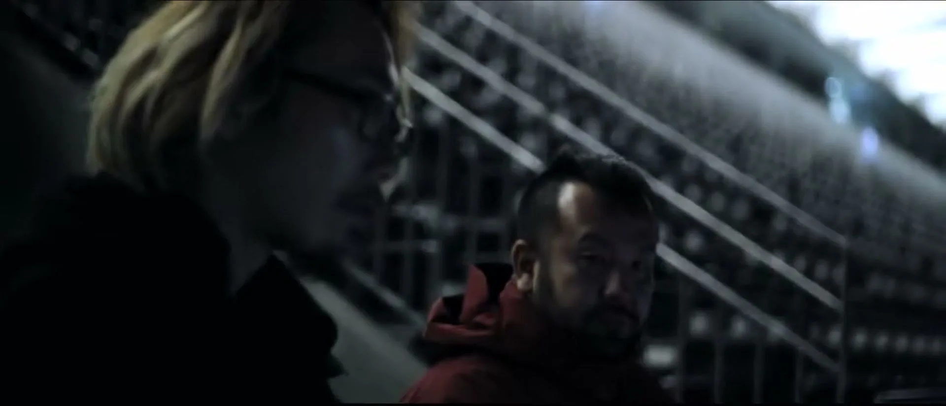 Two men, one with blonde hair and glasses, the other with a beard, sit in a dark, empty stadium at night.