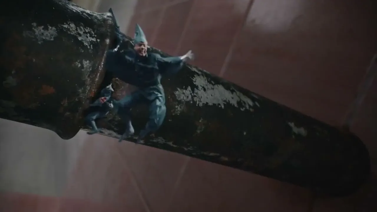 A tiny male figure in a blue uniform and hat struggles to climb out of a large, dark pipe, with other tiny figures visible inside, in a vast, industrial setting.