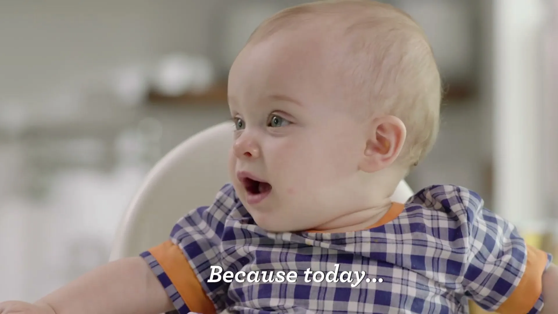 A baby in a high chair looks around with wide eyes and an open mouth, then turns to the side, in a bright kitchen.