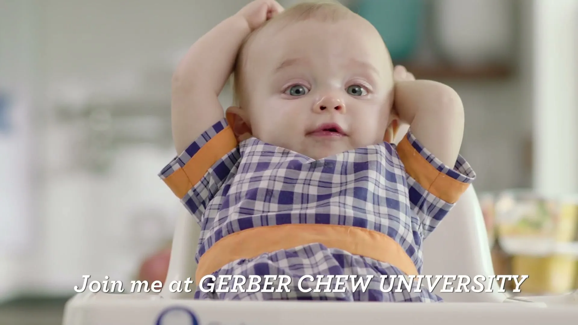 A baby boy in a high chair claps his hands and then puts them on his head, looking surprised in a kitchen.