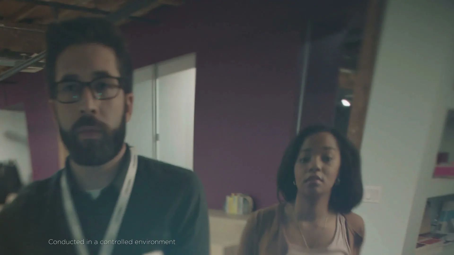 A man with glasses and a woman walk through a blurry, disorienting office space, experiencing a migraine.
