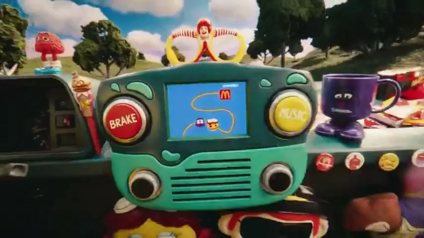 A toy-like game console with a screen showing a map and characters, surrounded by other colorful toys in a whimsical, outdoor setting.