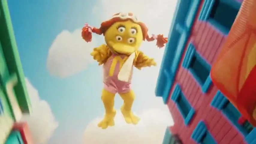 A purple monster with four eyes and a yellow smiley face character in a car, with a yellow four-eyed character floating above them in a colorful city street.