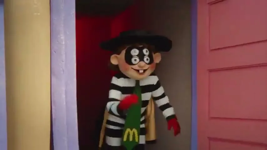 A stop-motion animated character, the Hamburglar, wearing a black and white striped outfit, black hat, and green tie, stands in a doorway.