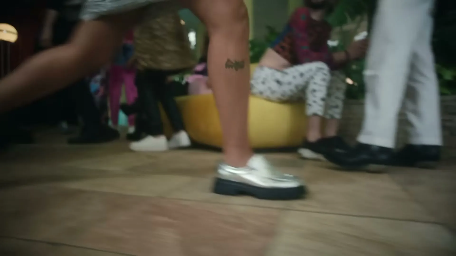 A low-angle shot captures the feet of several people dancing and moving around on a tiled floor at a party.