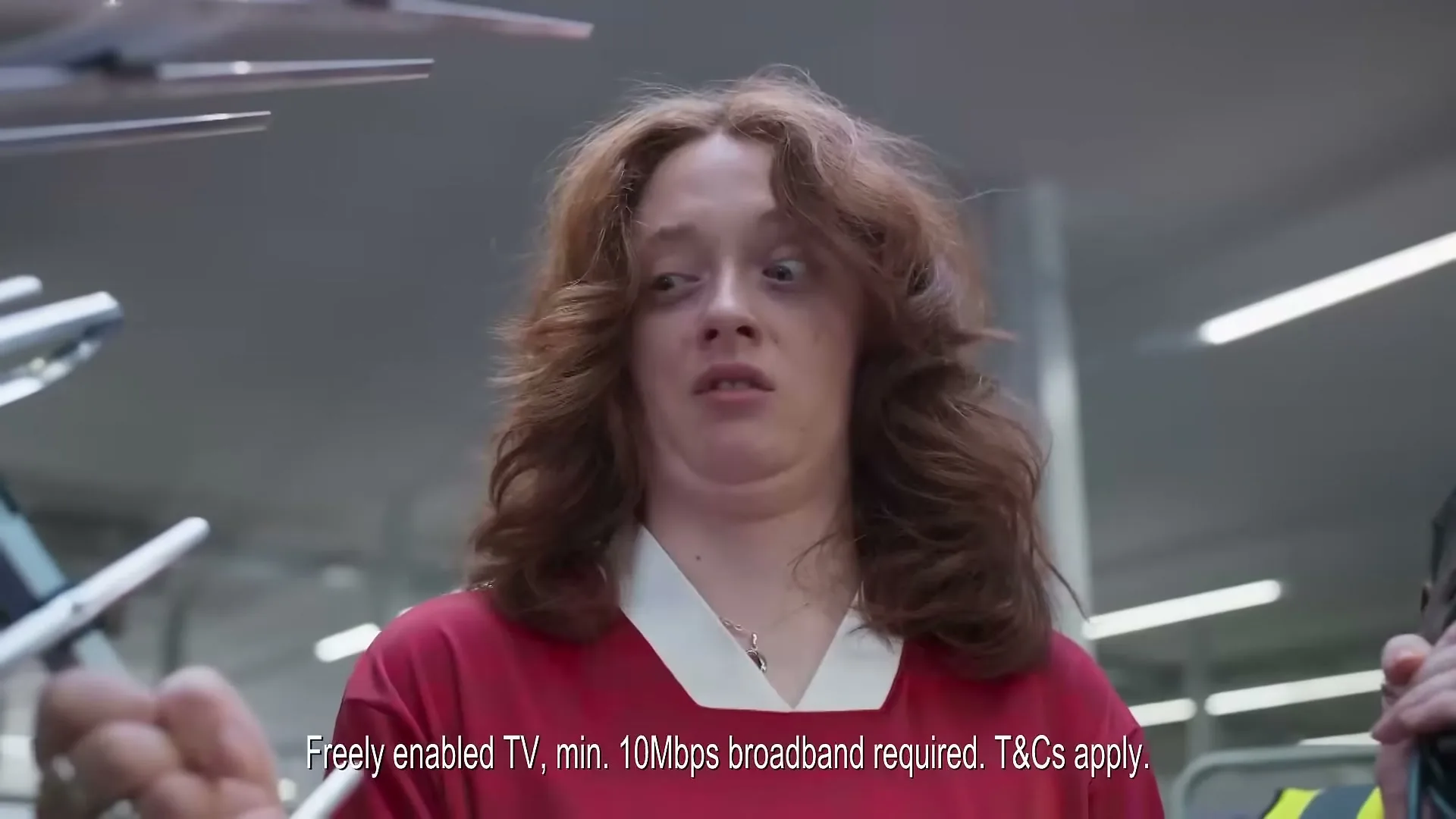 A young woman with red hair and a red shirt looks surprised and disgusted in a store, with legal text at the bottom.