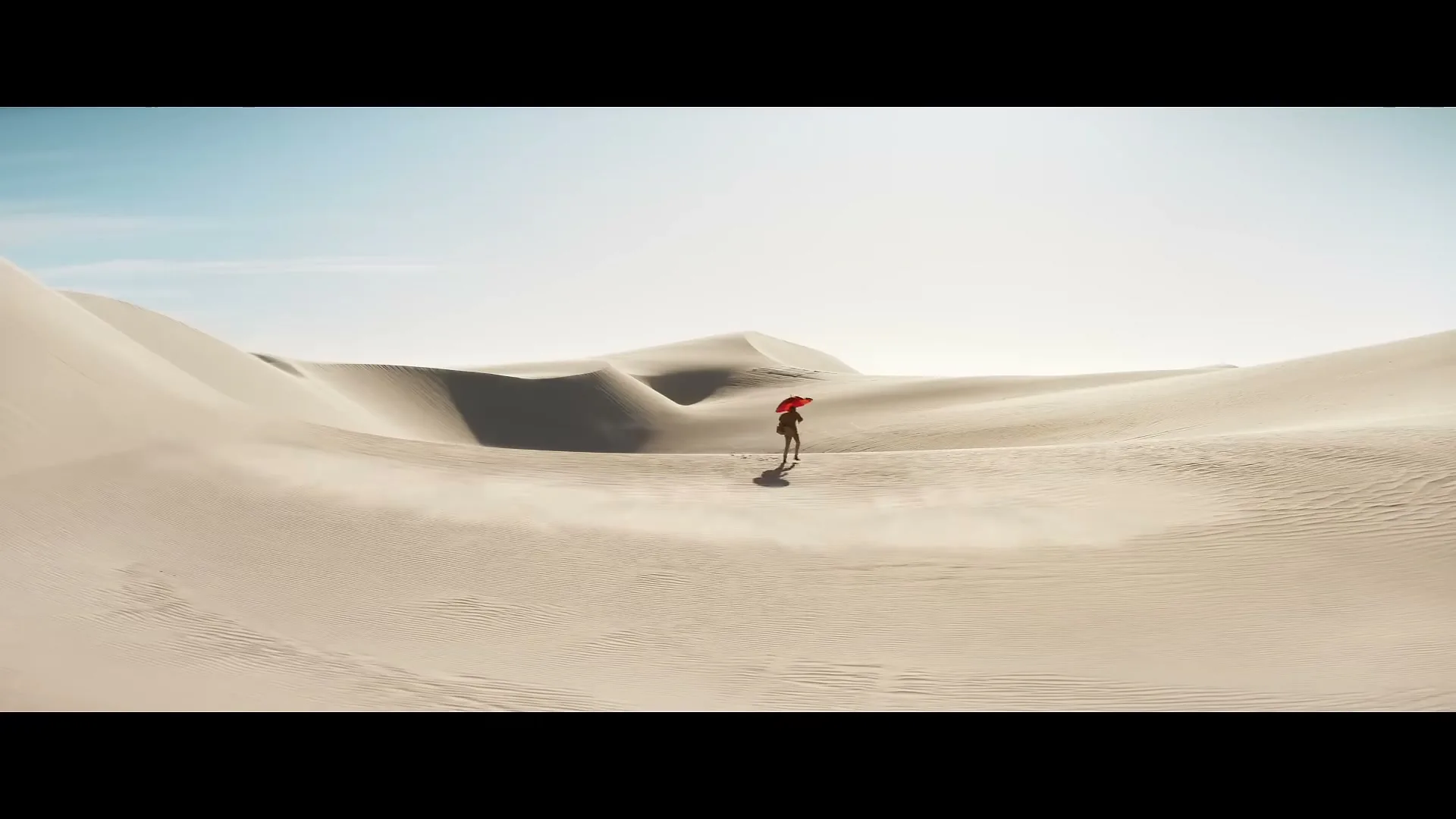 A lone figure, dressed in dark clothing and holding a red umbrella, stands in the middle of a vast, sun-drenched desert with rolling sand dunes under a clear sky.