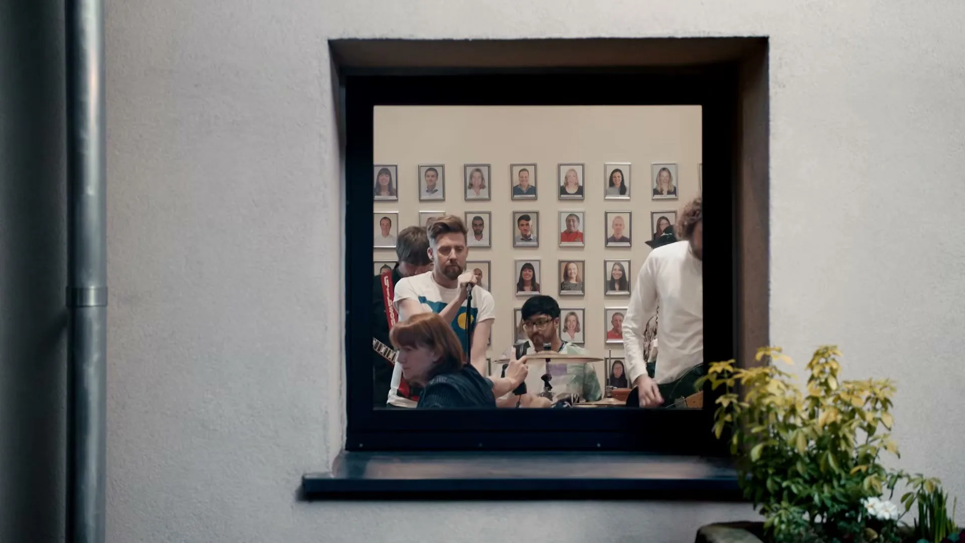 A wide shot of a window shows a group of people inside an office, with many framed photos on the wall behind them.