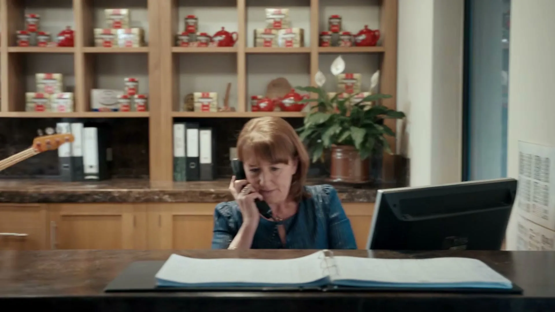 A rock band plays in an office, then the camera pans to a woman on the phone at a reception desk, with tea products on shelves behind her.