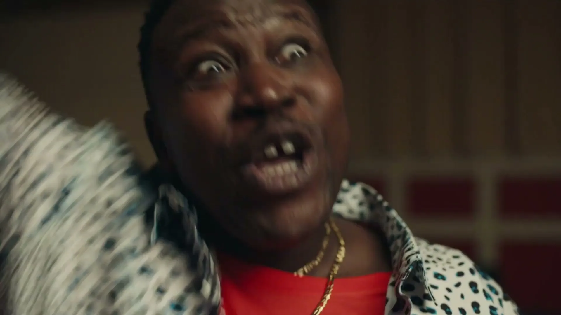 A man with a mustache and a leopard print shirt reacts with a surprised expression, opening his mouth wide in an interior setting.
