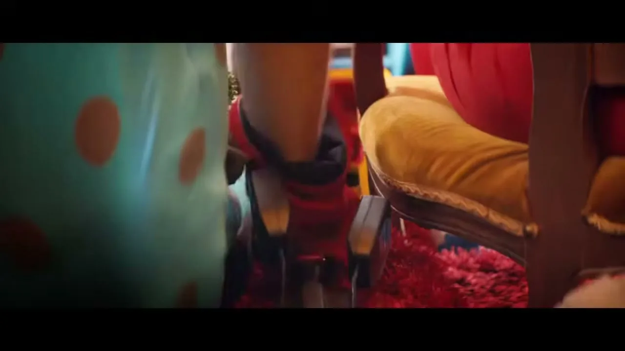 A clown's foot in a red shoe presses the accelerator pedal of a car, surrounded by colorful clown props and a fluffy red carpet.