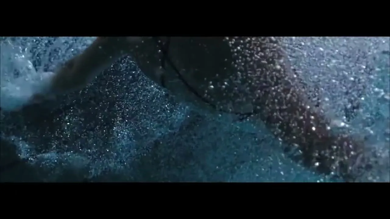 A person's arm and torso are seen underwater, covered in bubbles, as they swim in a dark pool.