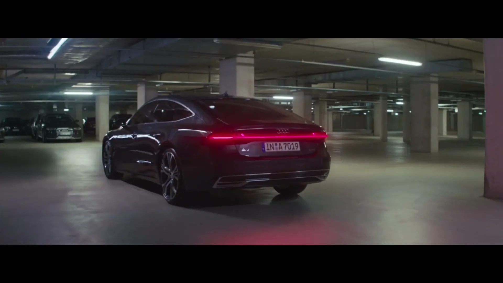A dark Audi car with illuminated taillights is parked in a dimly lit underground parking garage.