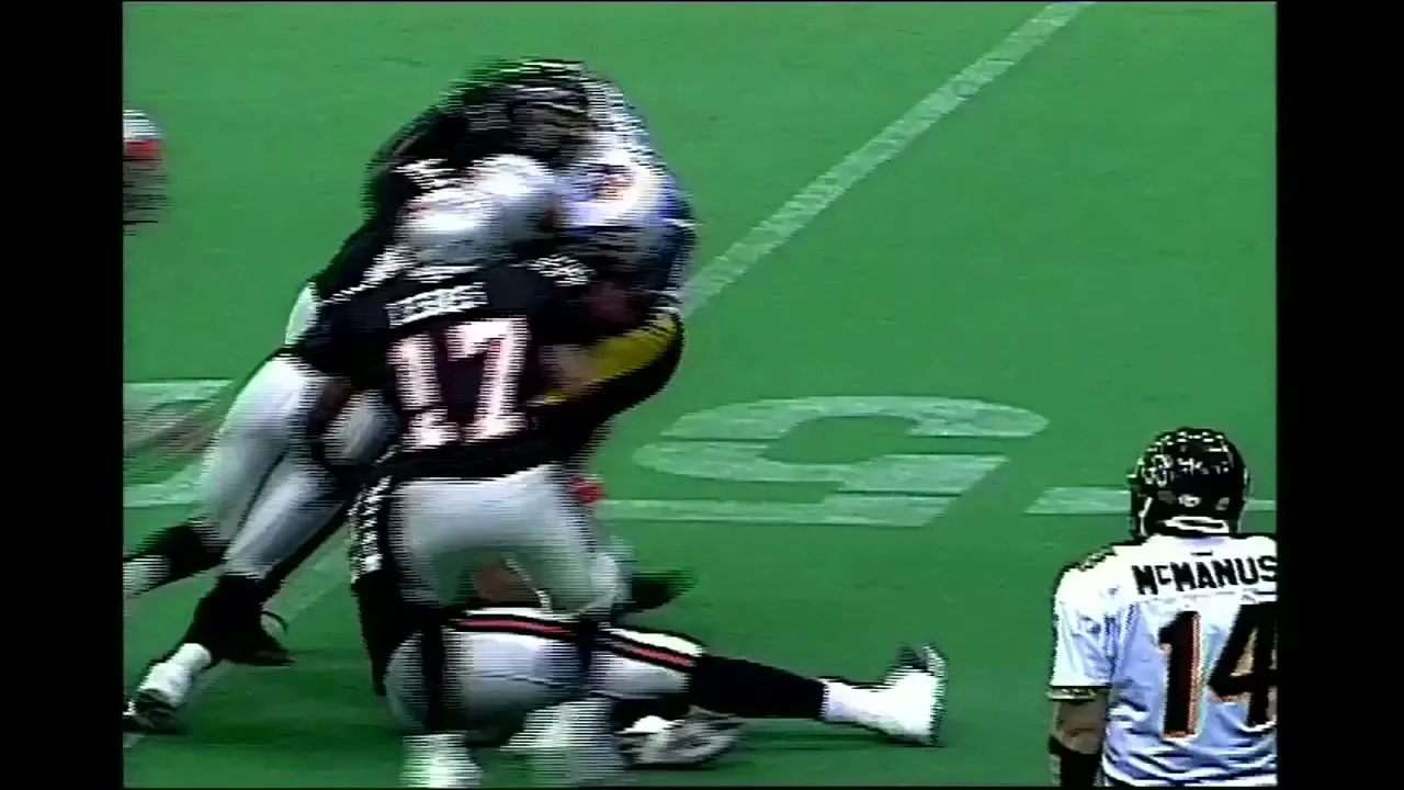 Football players in black and white uniforms tackle each other on a green field during a game.