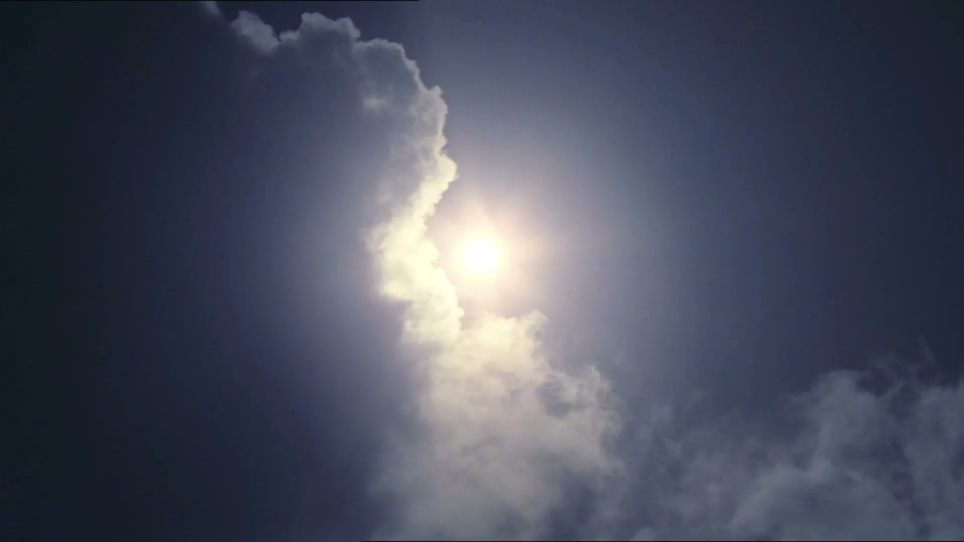 The bright sun shines through a gap in dark clouds, creating a dramatic and serene sky view.