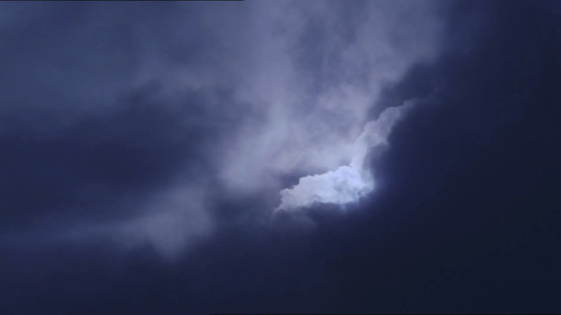 A bright light shines through dark, ominous clouds, creating a dramatic and mysterious sky.