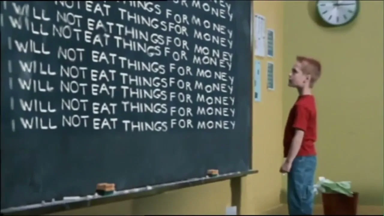 A young boy in a red shirt and blue jeans writes "I will not eat things for money" on a blackboard, then runs out of school and skateboards away.