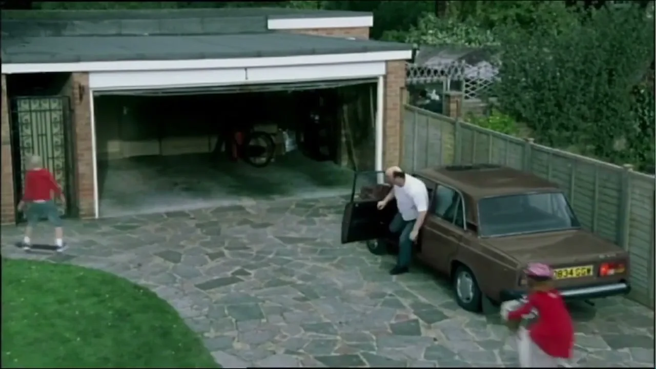 A family arrives home, with a boy on a skateboard, a girl running, and a man getting out of a car, as a garage door opens.