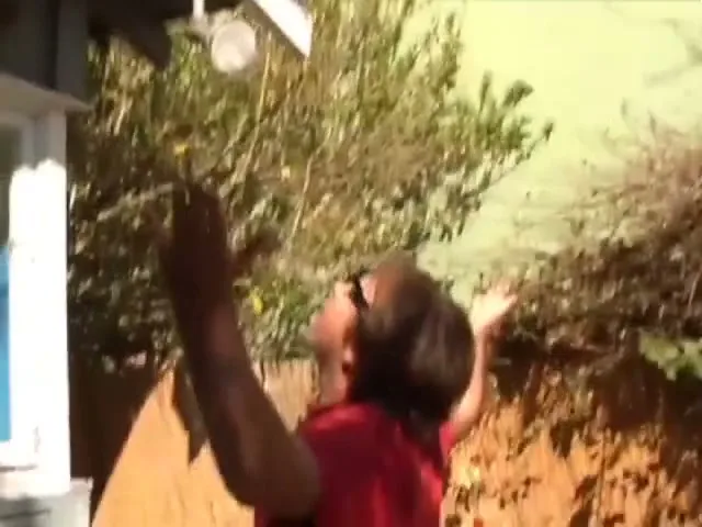 A man on a roof drops sunglasses, which are caught by another man below, who then high-fives the camera.