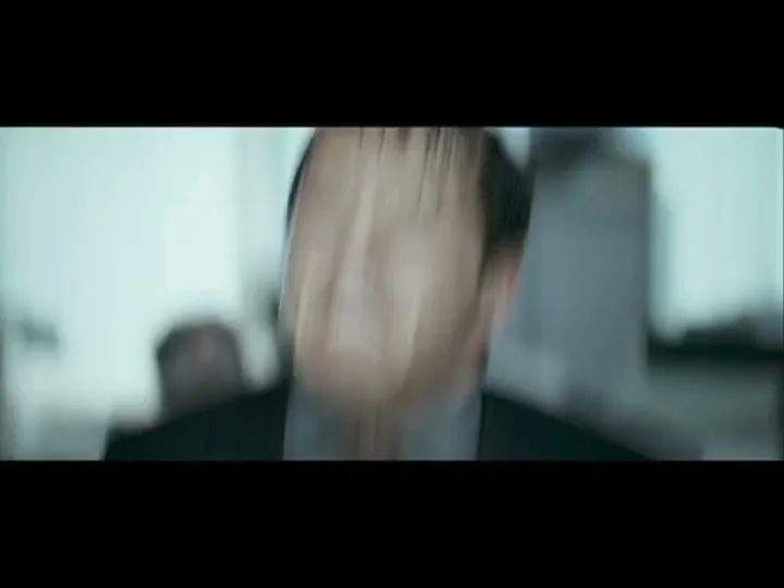 A man in a suit screams in frustration, his face contorted, as he struggles against an unseen force in a brightly lit office.