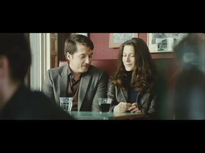 A man and a woman sit at a table in a restaurant, looking at each other and talking.
