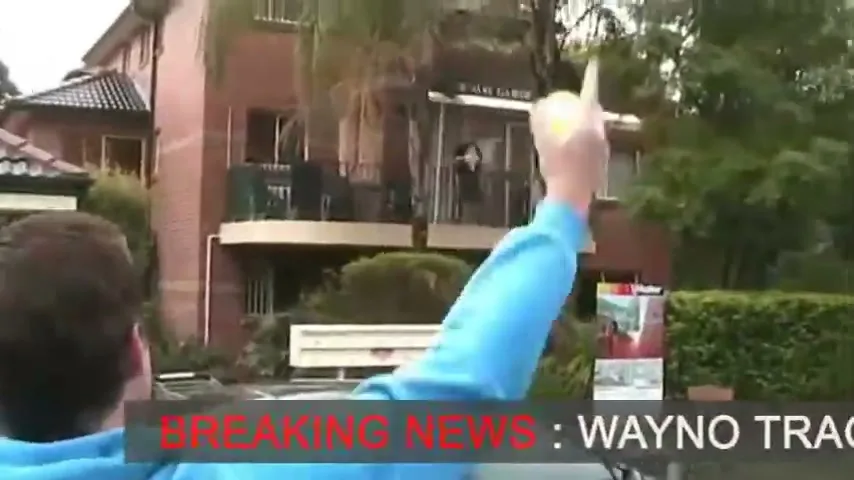 A man in a blue hoodie holds a Gatorade bottle, then points up at another man on a balcony, who is holding a tennis racket.