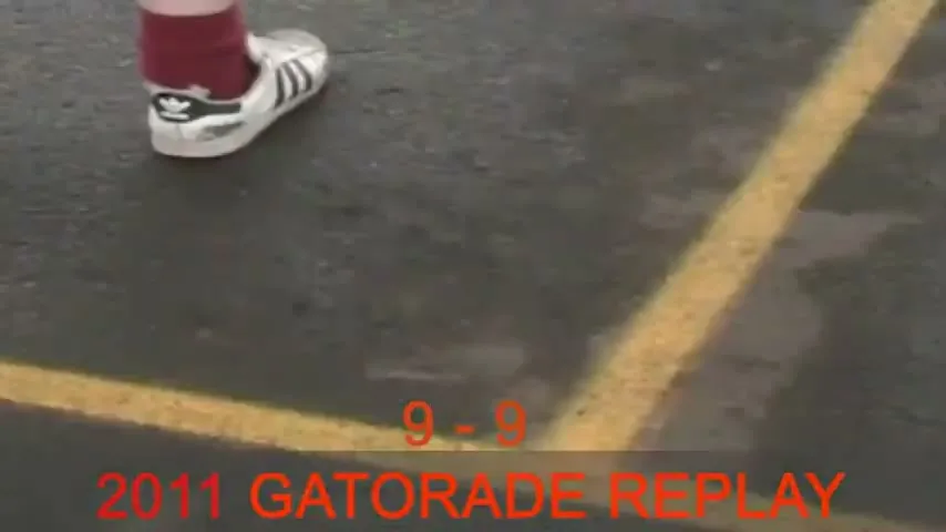 A person's foot in a white Adidas shoe and red socks stands on a wet asphalt court with yellow lines, as a tennis ball bounces nearby.