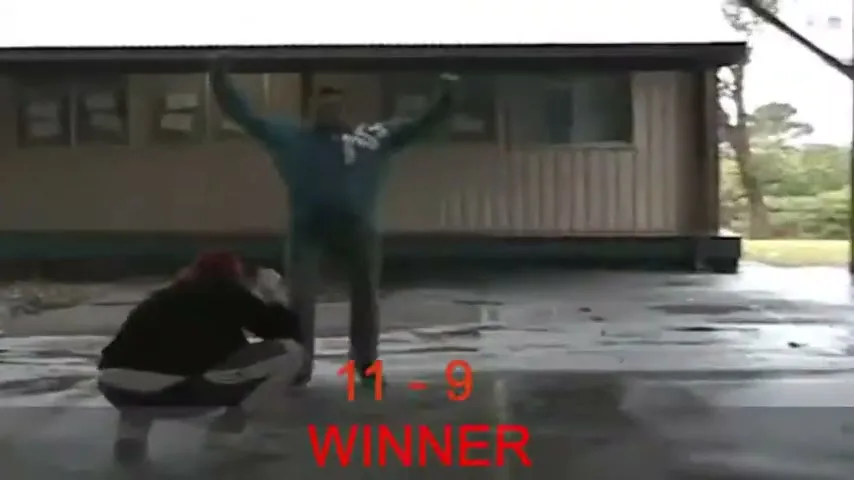 Two men play a game on a wet outdoor court, one celebrates a win while the other kneels in defeat, with score text overlaid.